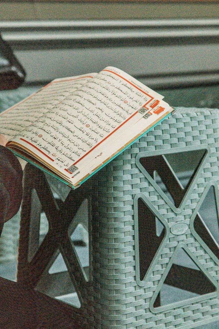 An open Quran placed on a woven plastic stool inside a room.