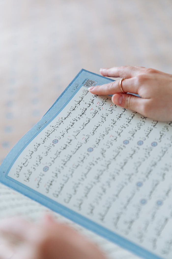 Close-up of a hand holding an open page of the Quran, emphasizing Islamic faith and study.