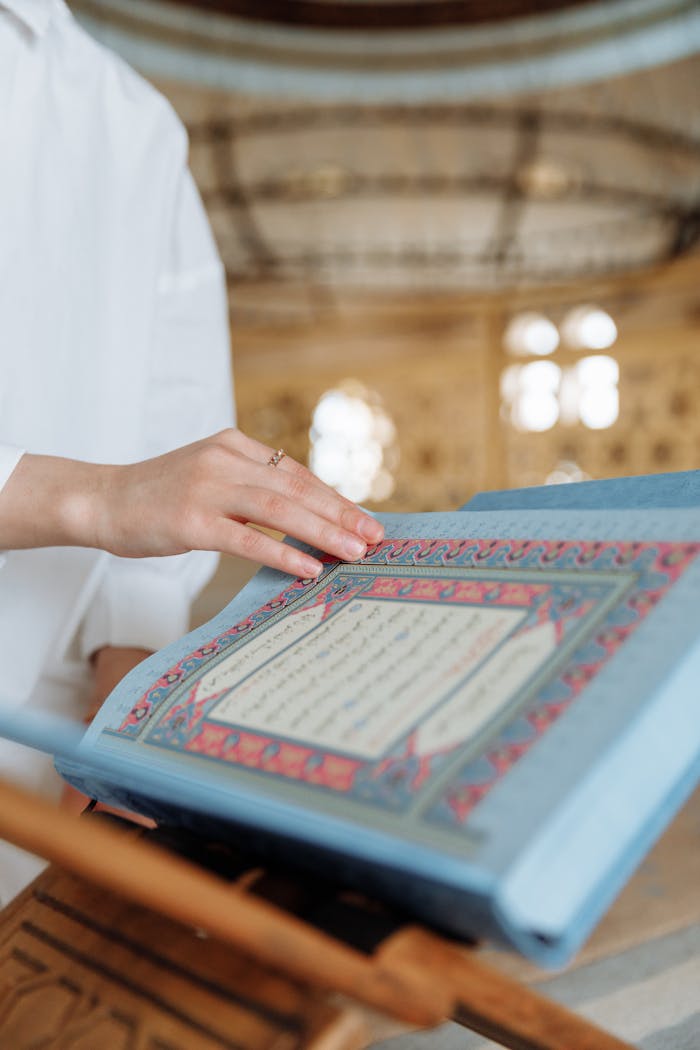 A person touches an open Quran inside an ornate mosque, symbolizing faith and spirituality.